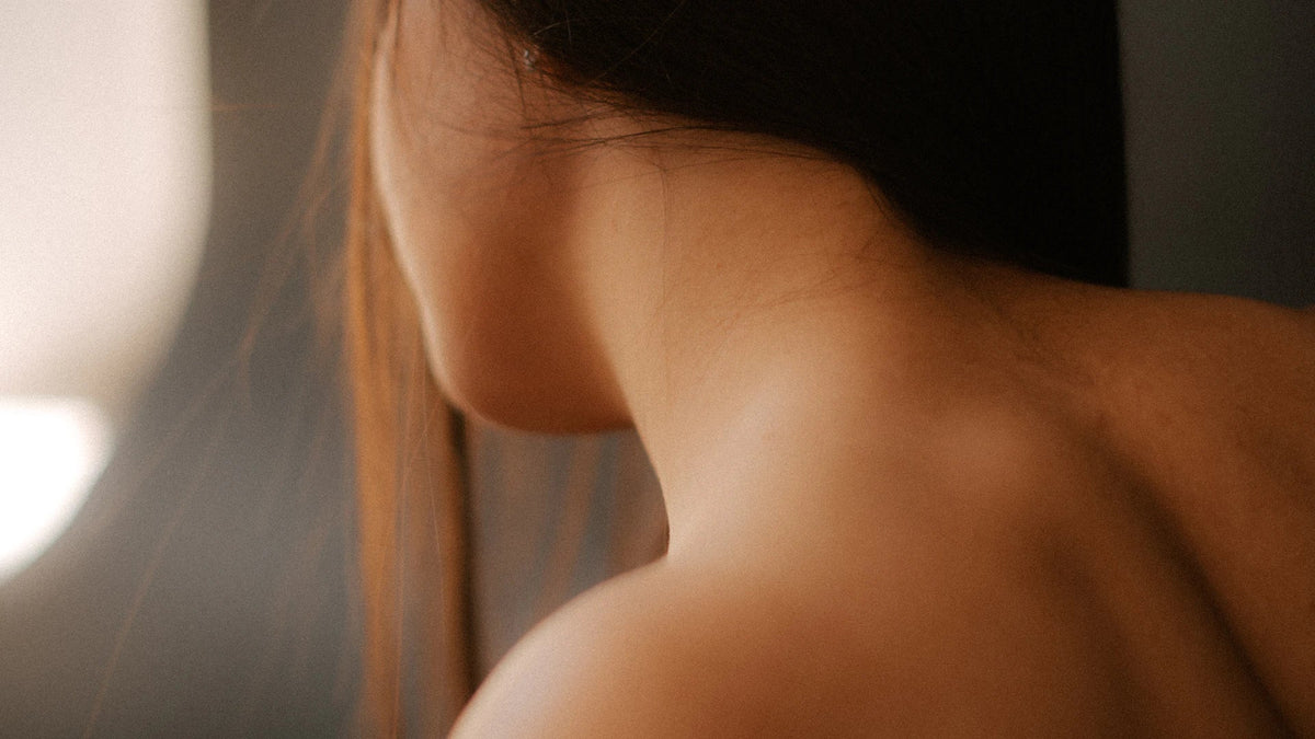 An adult woman's shoulder and back in soft natural light, without a visible face.