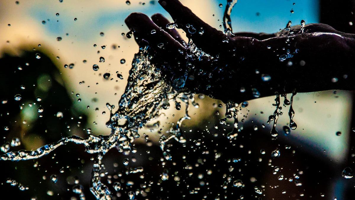 Hands rinsing under splashing water outdoors.