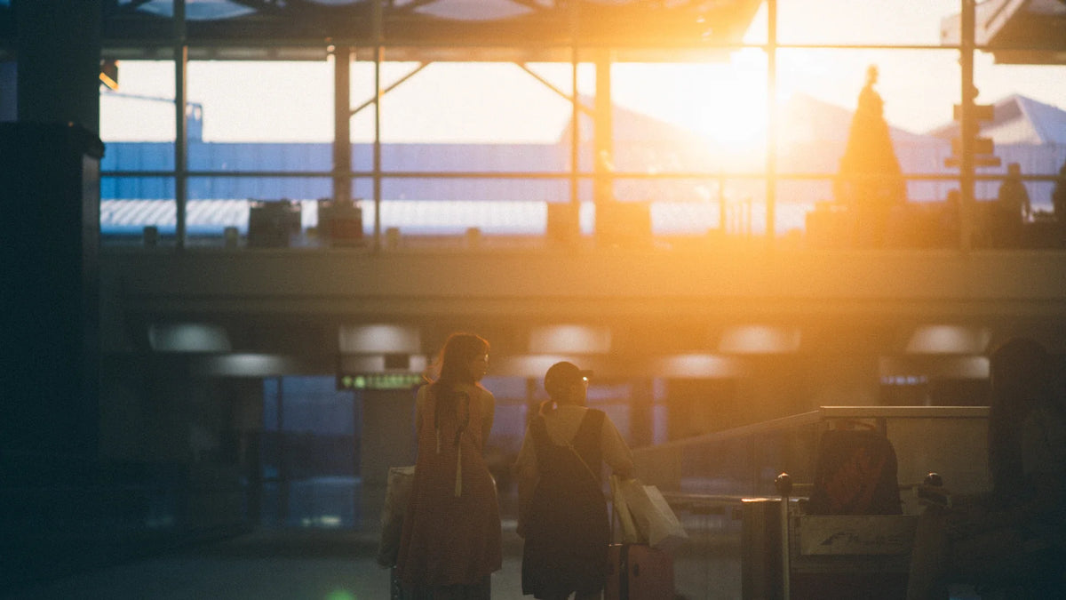 Two women walking with luggage through an airport lit by the rising sun.