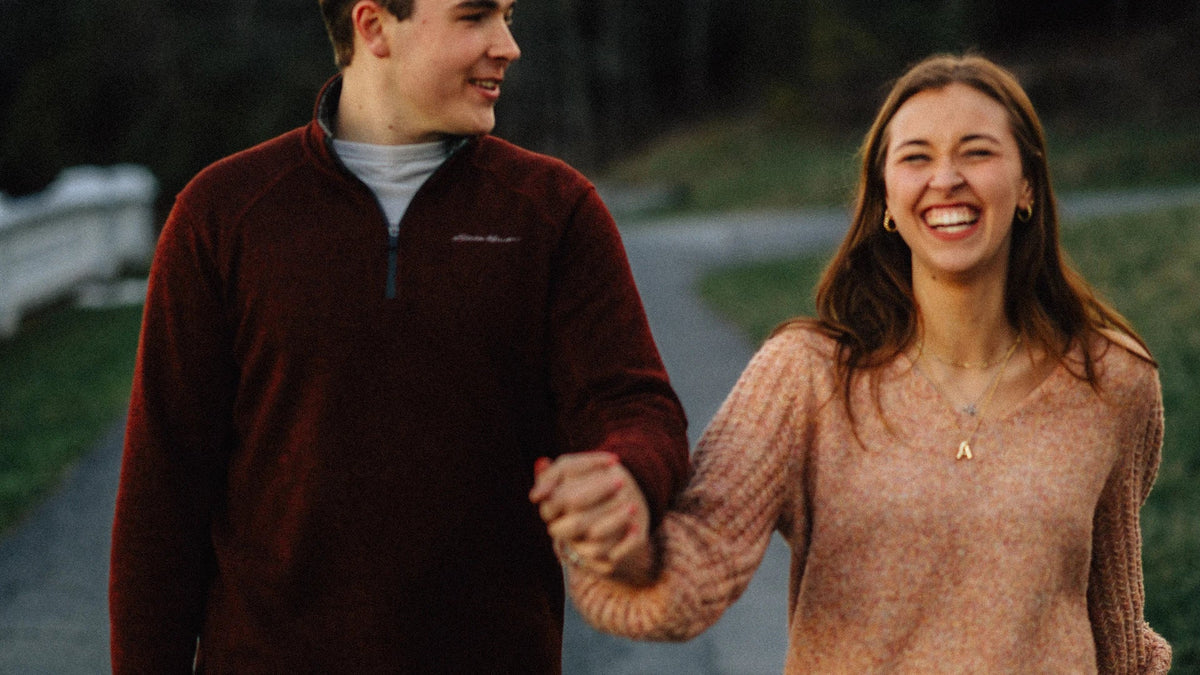 An adult couple smiles while walking hand in hand outdoors.