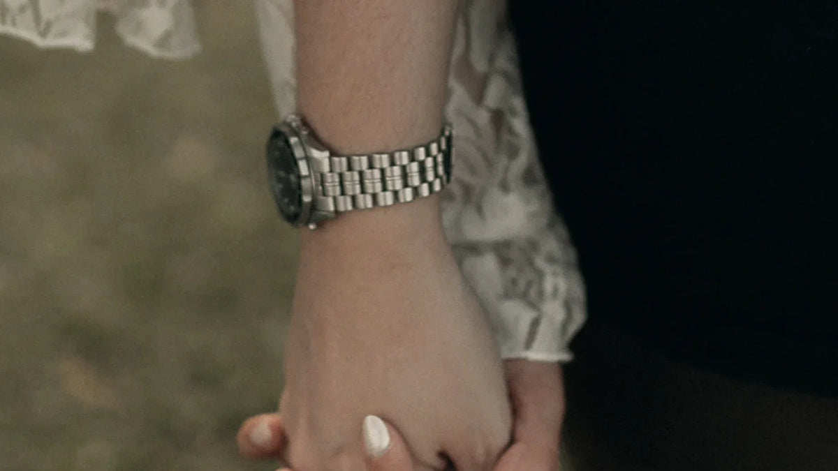 Cropped view of adult companions holding hands, with lace fabric and dark clothing.