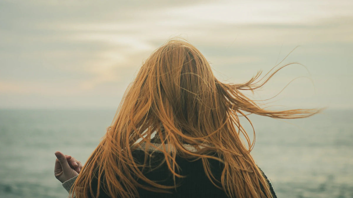 A woman faces the sea, seen from behind.
