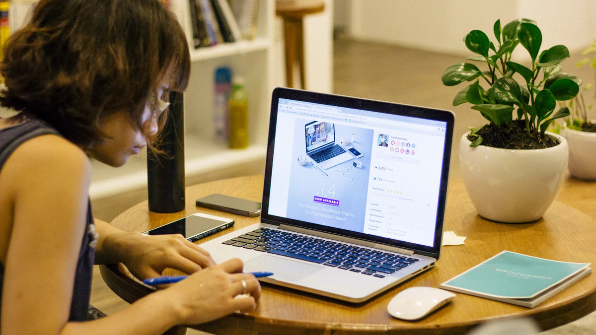 A woman uses a laptop while taking notes at a table.