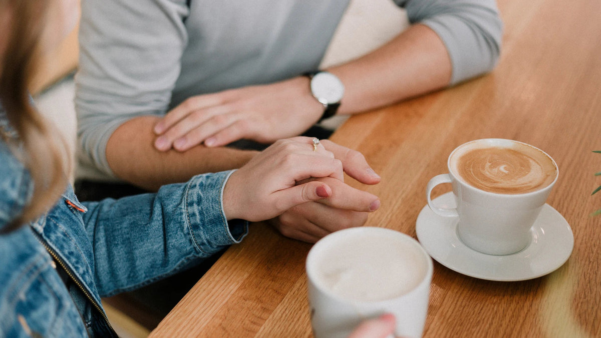Two adult hands are held together at a cafe table.