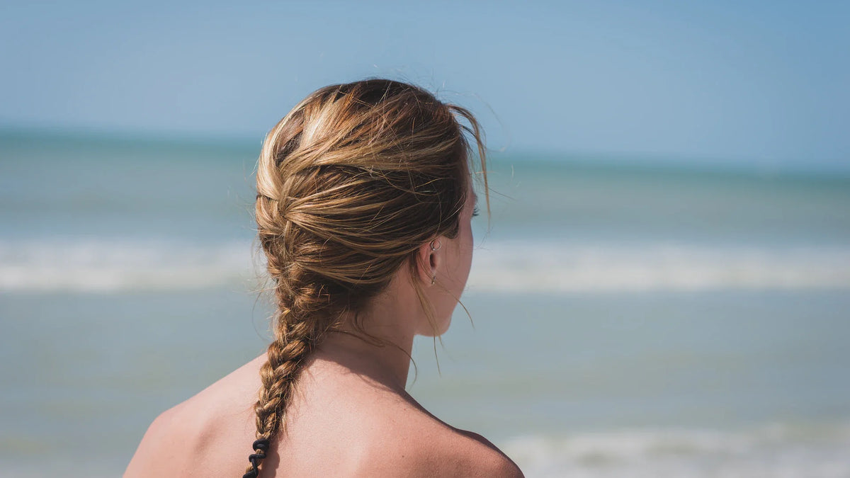 An adult woman viewed from behind beside the sea.