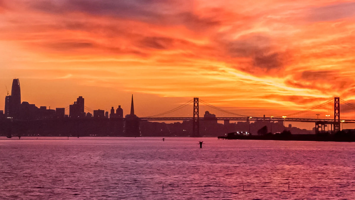 An orange sunset over water and a city skyline.