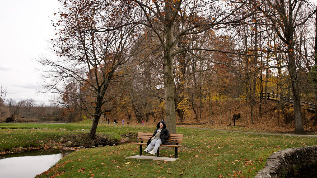A woman sits alone on a bench in an autumn park.