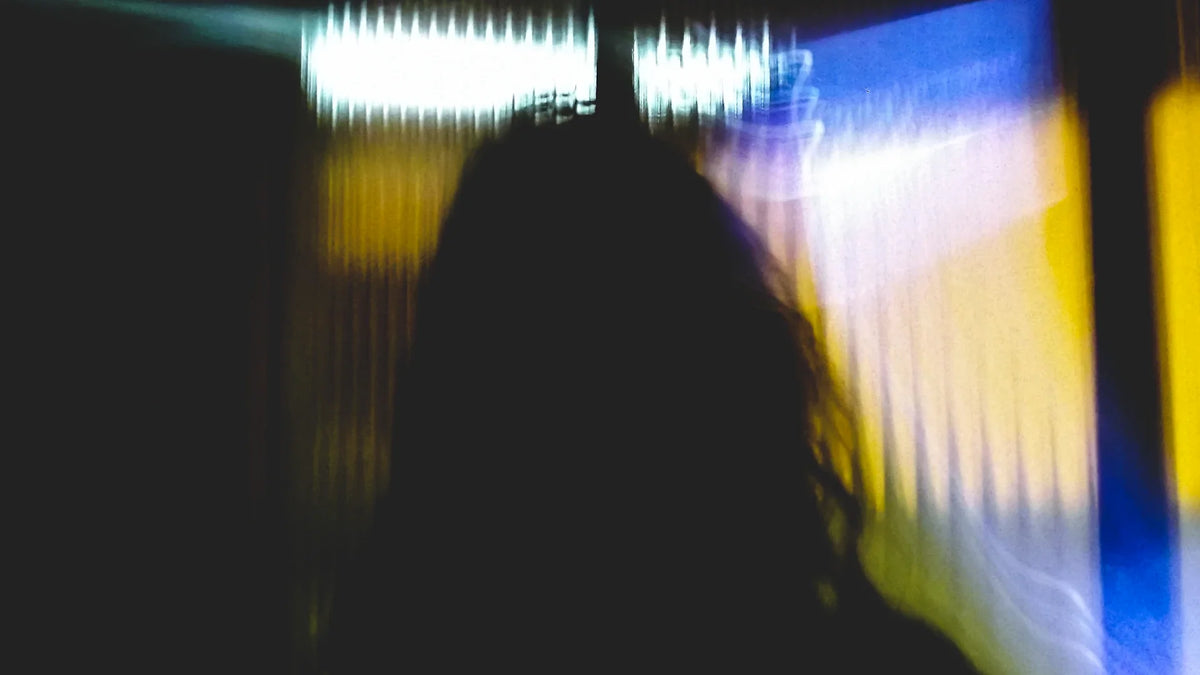 A blurred adult silhouette seen from behind against coloured window light.
