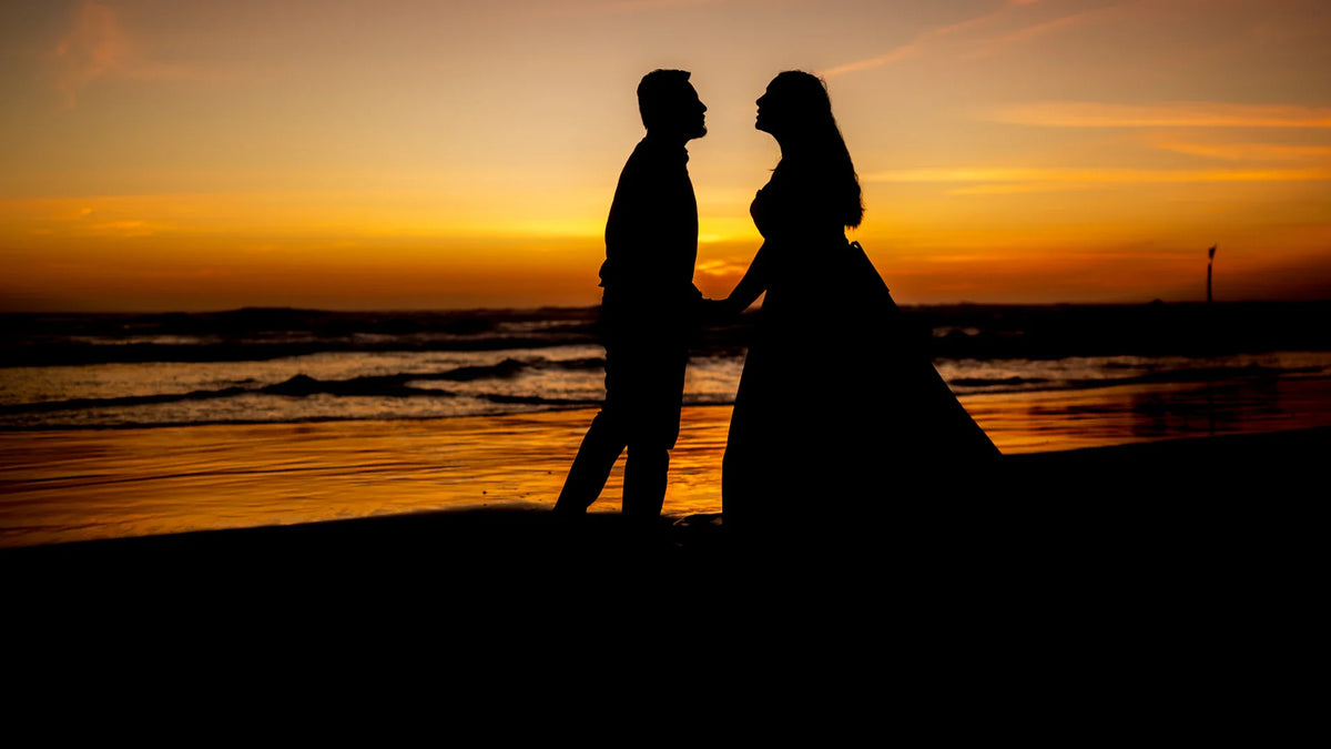 An adult couple holding hands on a beach at sunset.