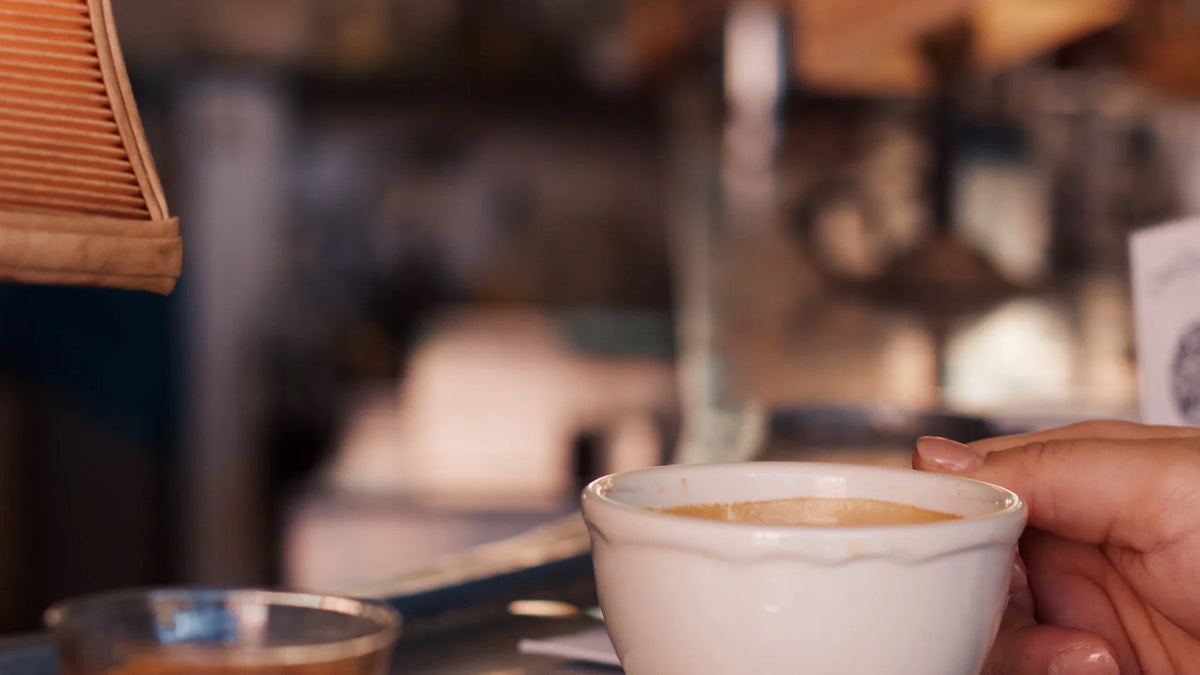 A hand rests beside a coffee cup in a café.