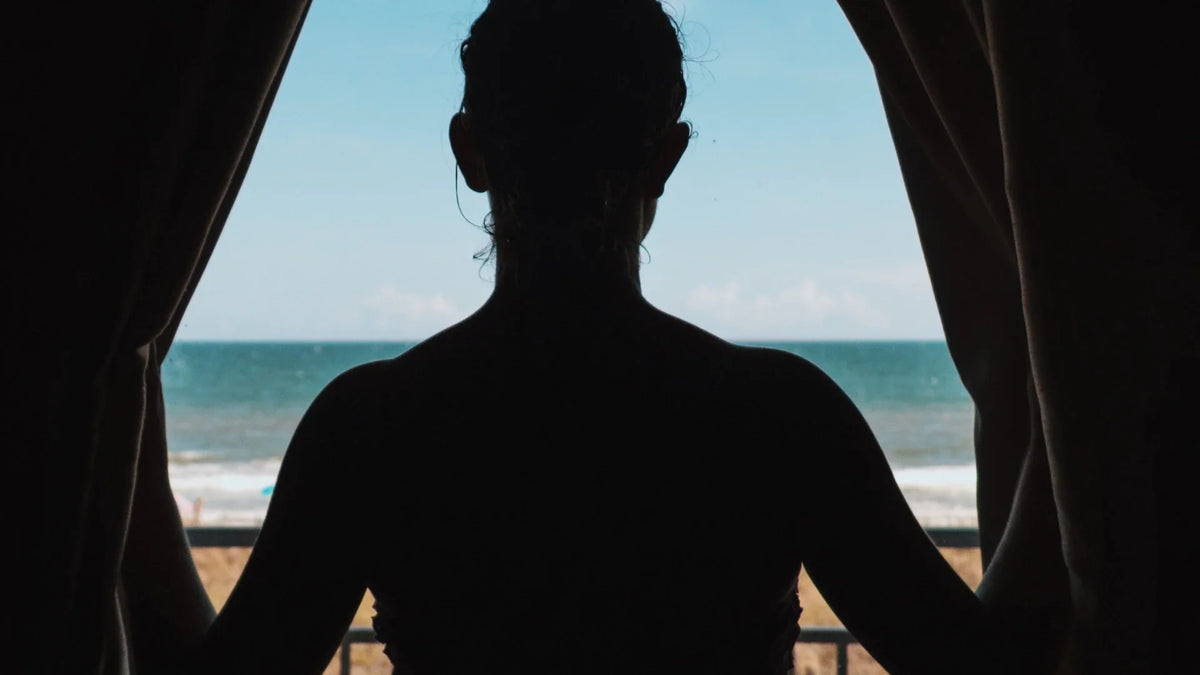 An adult woman seen from behind as a dark silhouette between curtains.