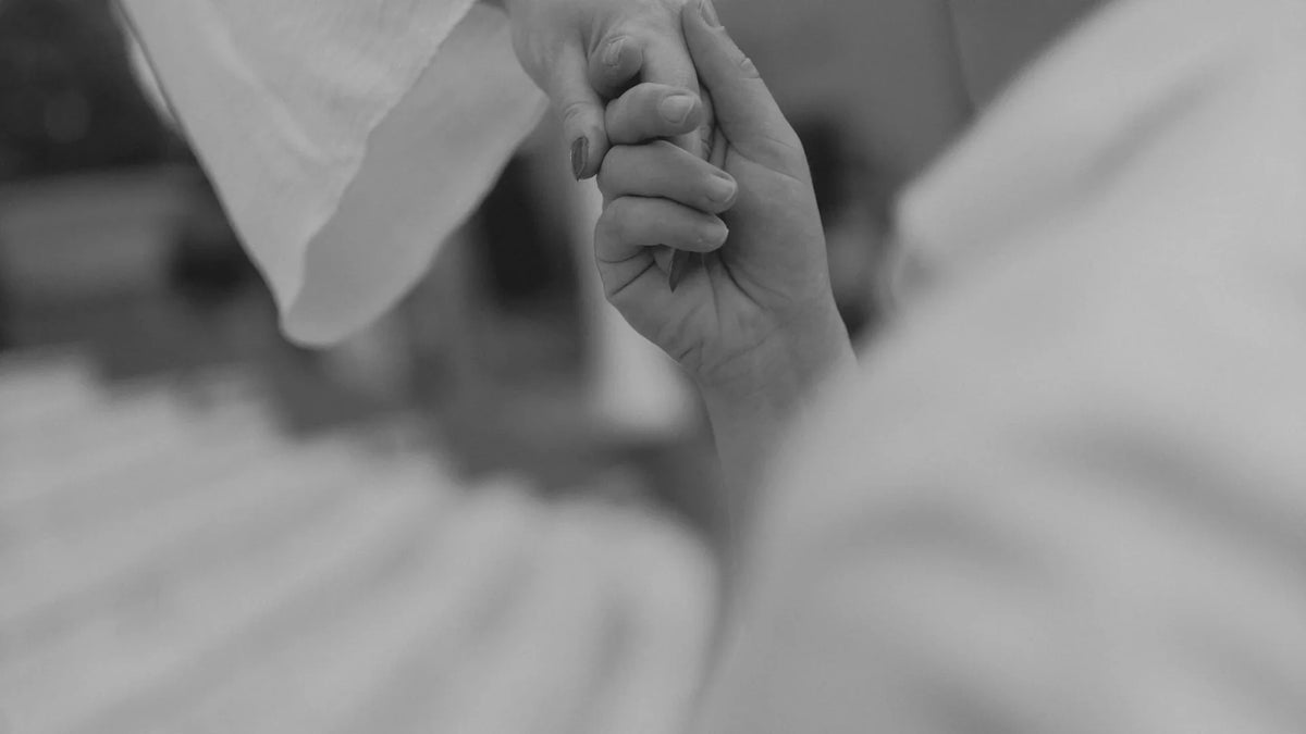 A black-and-white close-up of two adults holding hands.