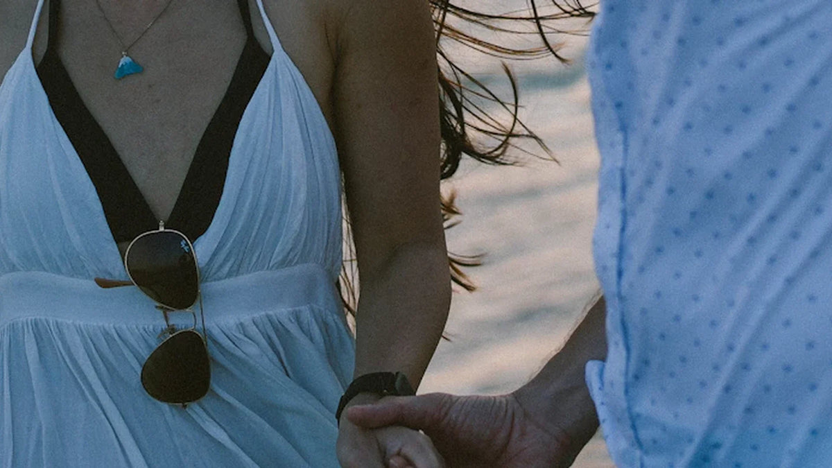Cropped view of adult companions holding hands beside the sea.