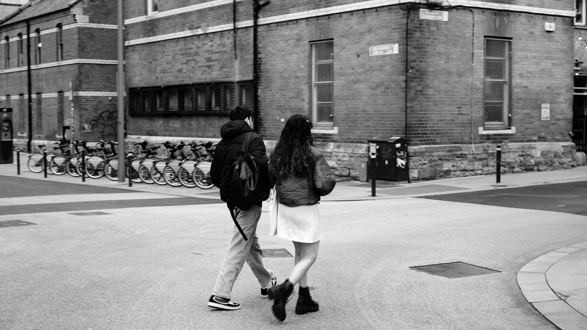 Two adults seen from behind walking along a city street in black and white.