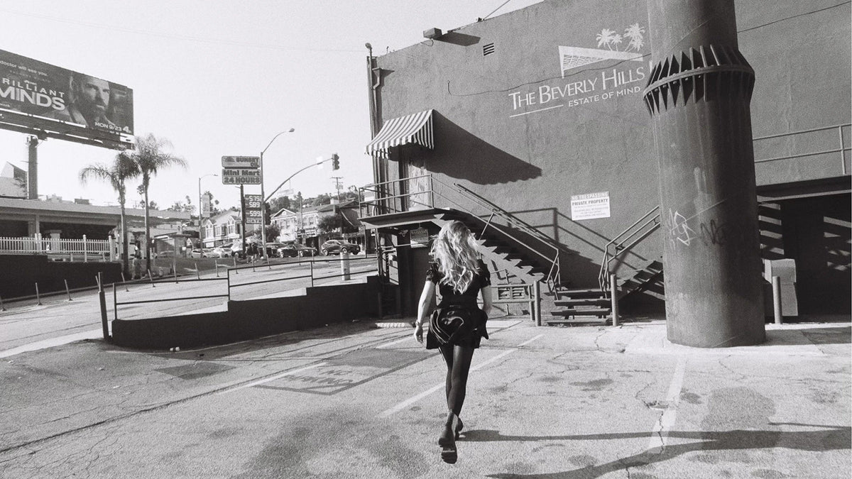 An adult woman walking away along a city pavement.