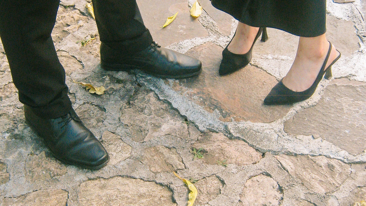 Two adults’ shoes and lower legs on a stone path.