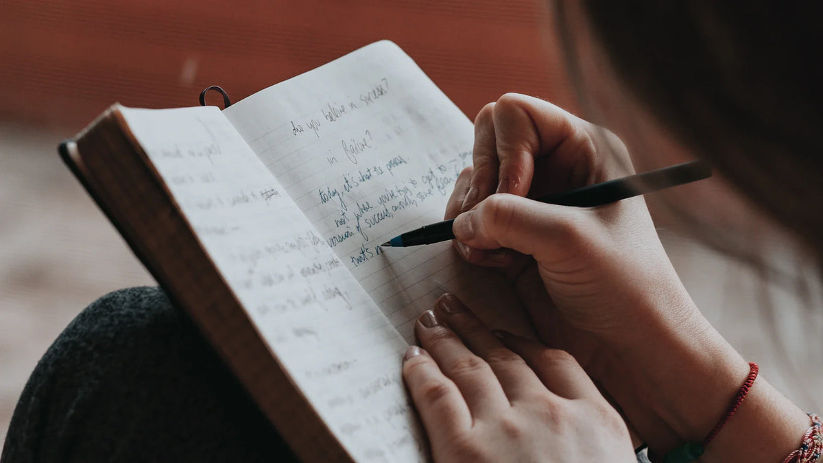 A woman writes in a notebook with a pen.