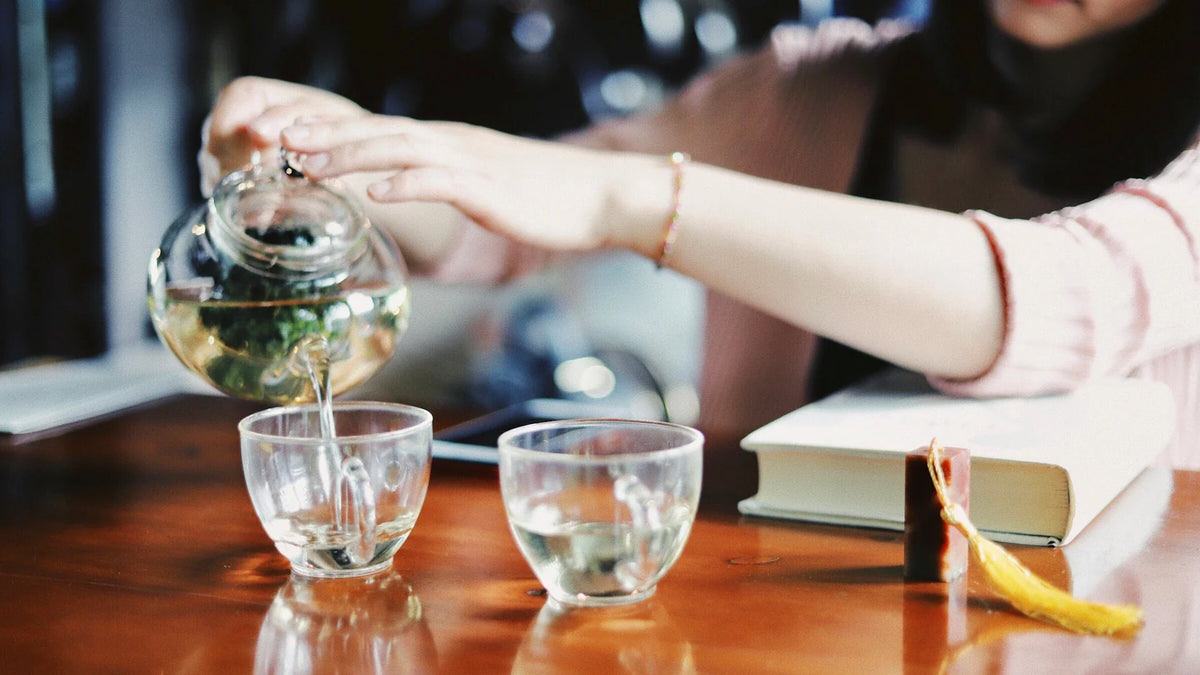 An adult woman pouring tea into glass cups at a table, with her face outside the frame.