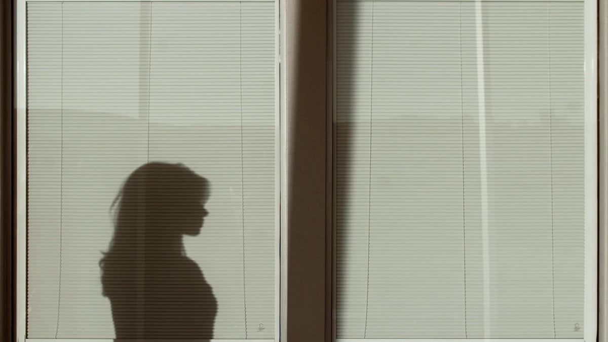 A woman’s shadow cast on a pale window blind.