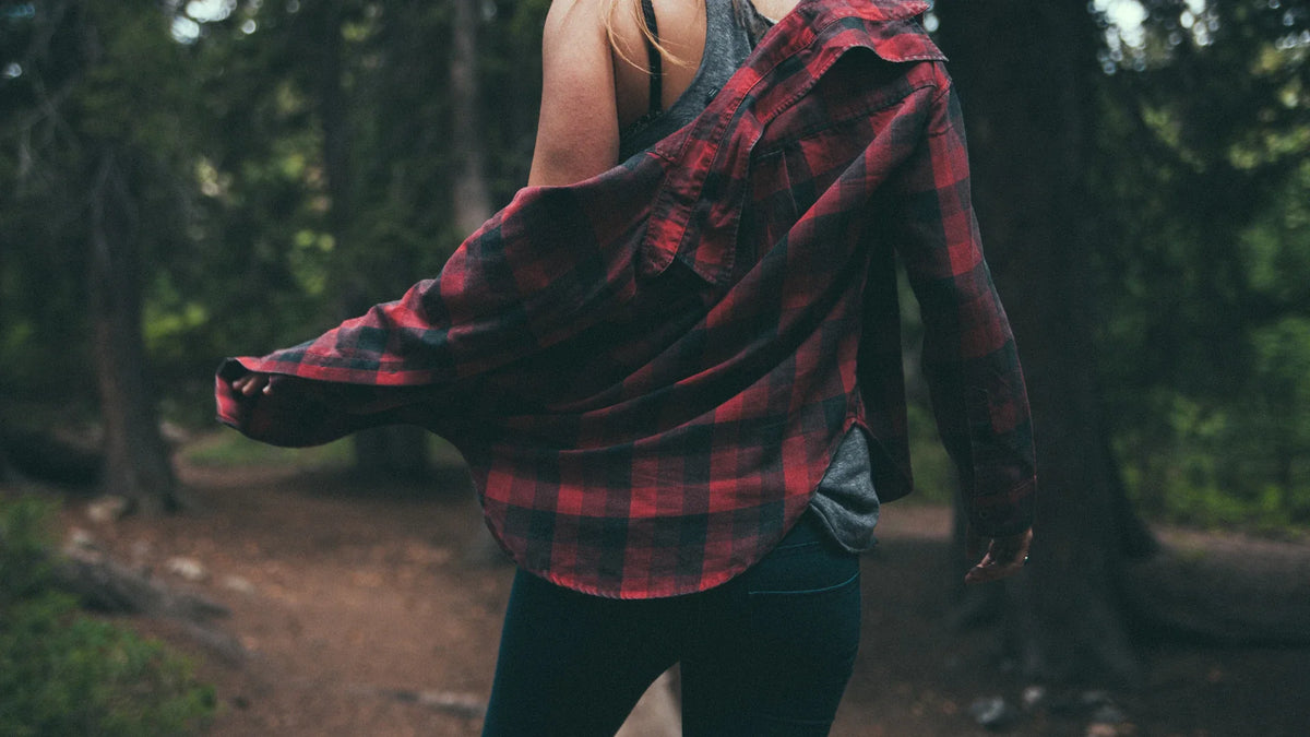 An adult woman in a shirt viewed from behind between tall trees.