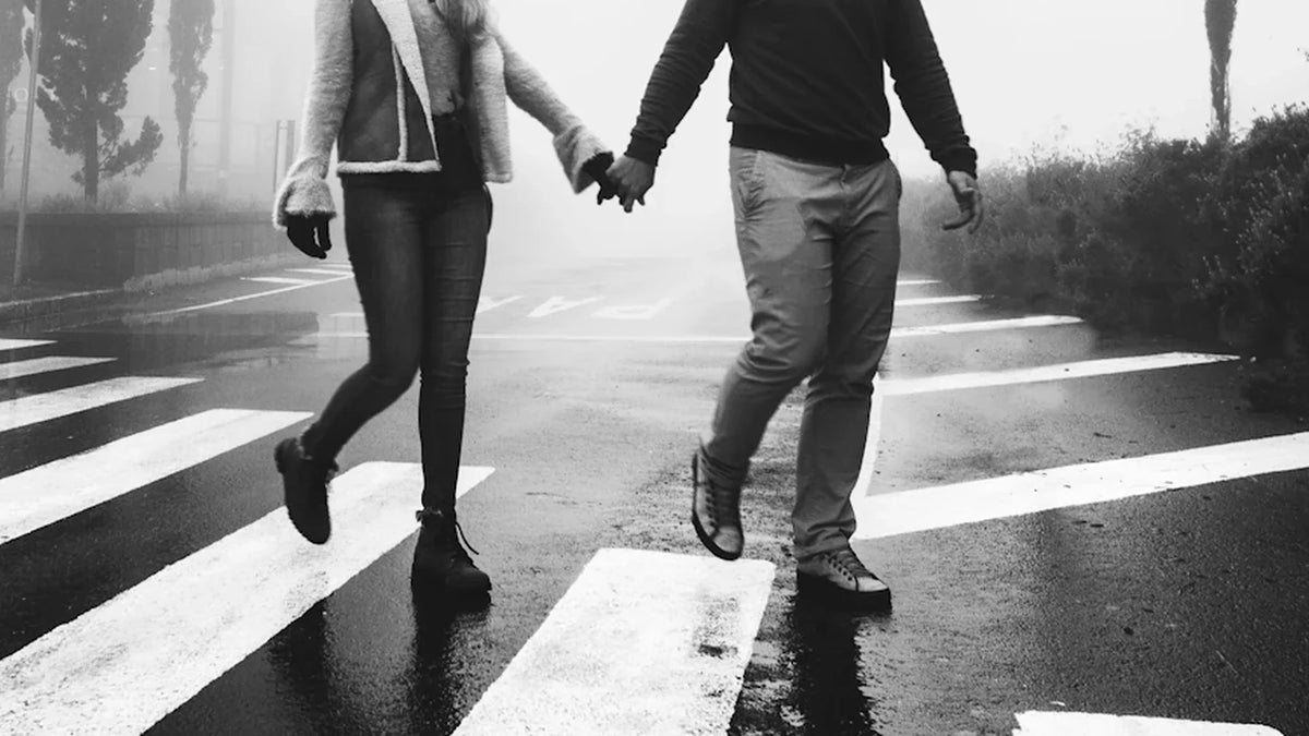 Cropped view of adult companions holding hands while crossing a street.
