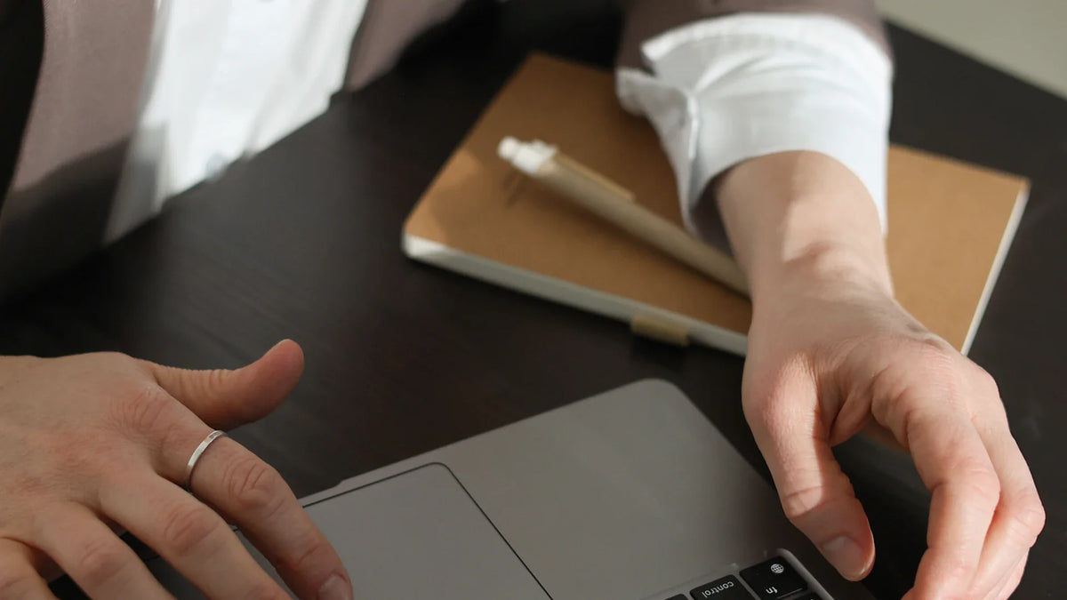 Hands rest on a laptop beside a notebook.