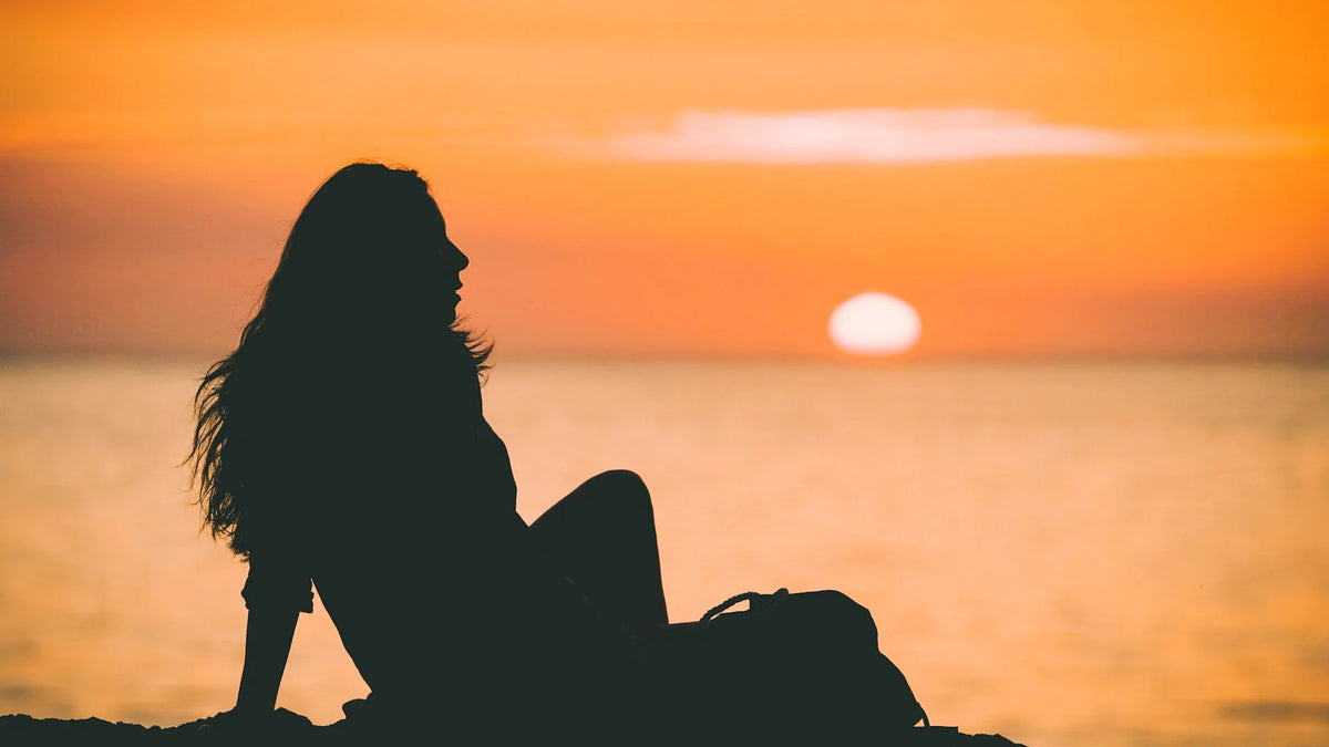 An adult woman silhouetted beside the sea.