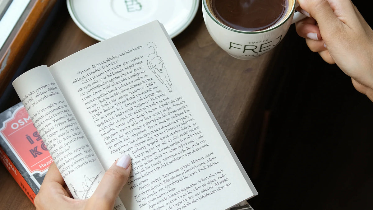 Hands hold an open book beside a cup of coffee.