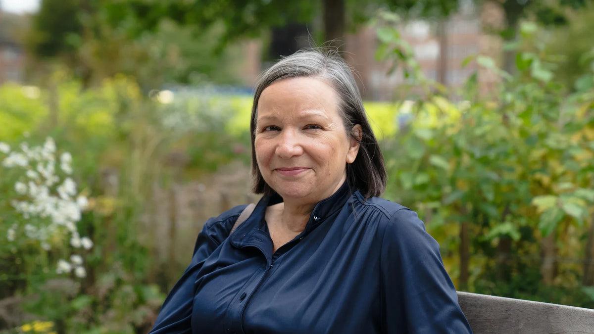 A mature woman smiles while sitting outdoors in a park.