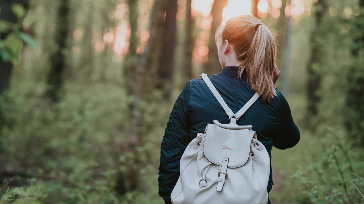 An adult woman walking along a forest path, viewed from behind.