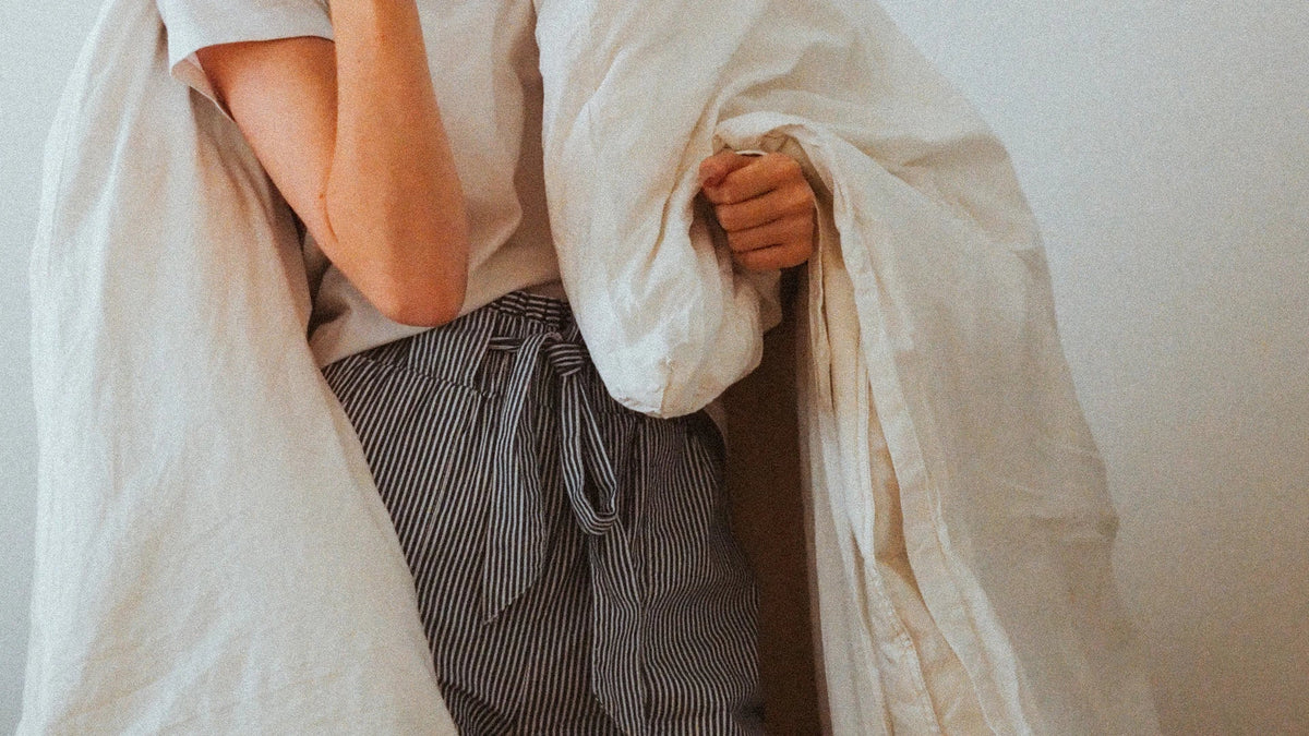A woman wrapped in white bedding during a quiet moment at home.
