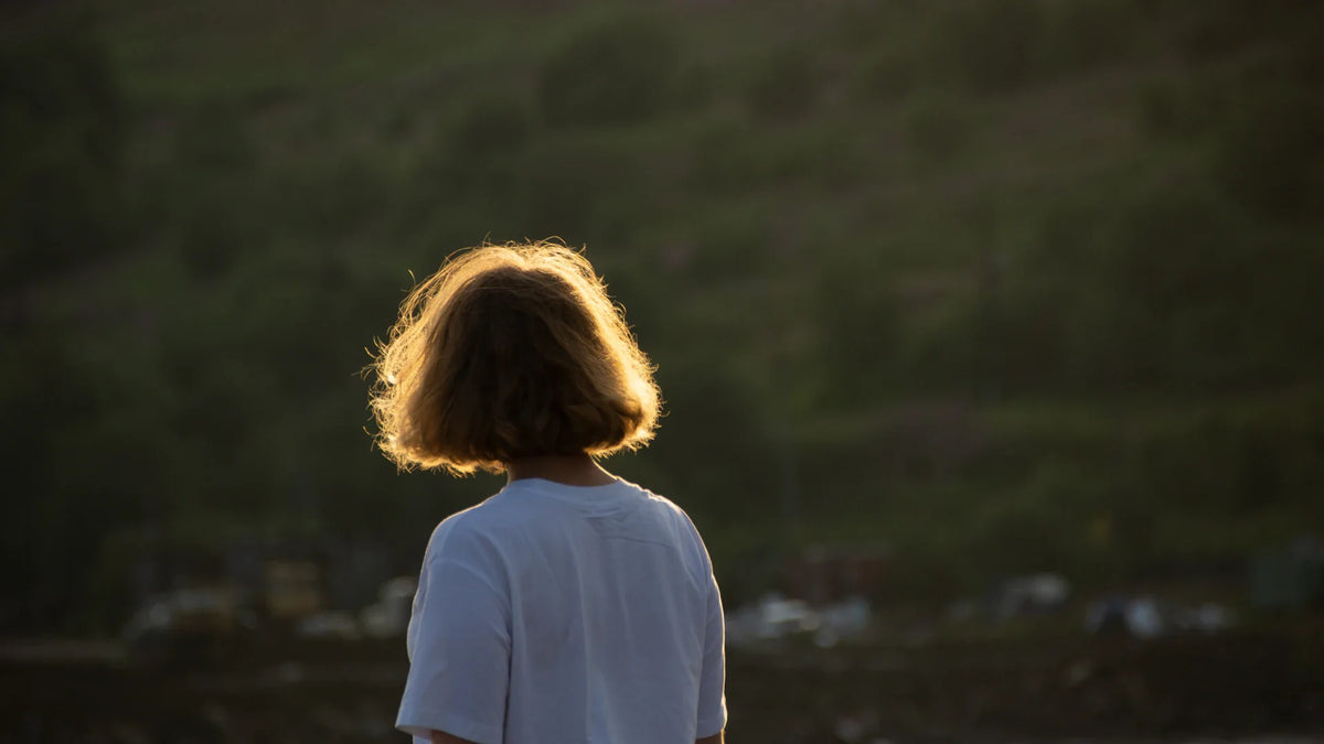 A woman in a white shirt seen from behind in warm evening light.
