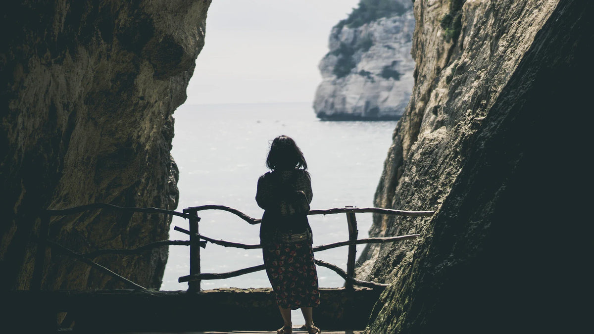 A woman seen from behind looking across a coastal cove.