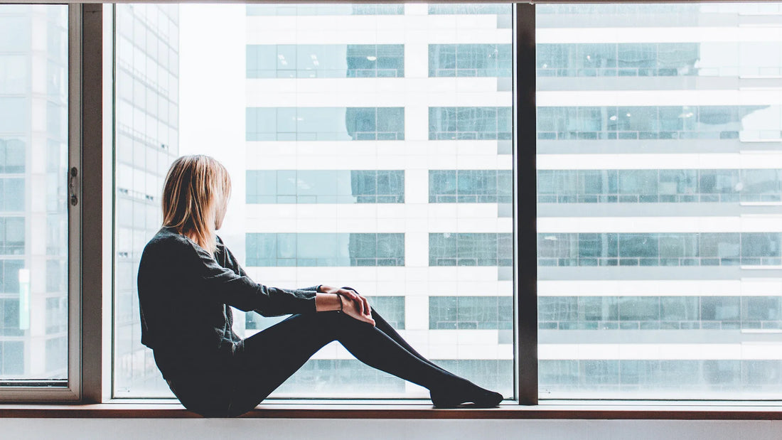 A woman seated beside a large window in a quiet moment.