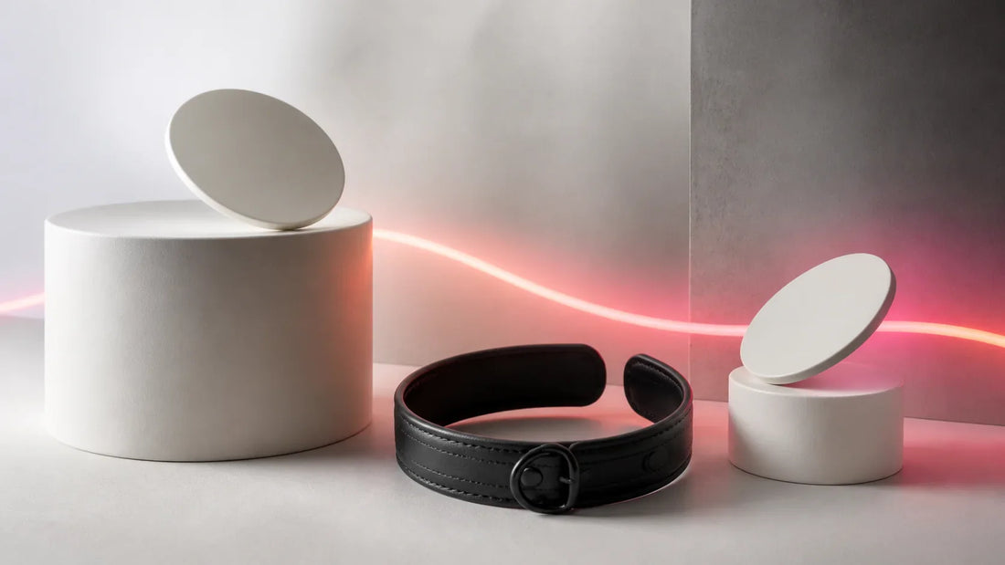 Two blank ceramic name tokens, an open black collar and a coral light line on a neutral studio set