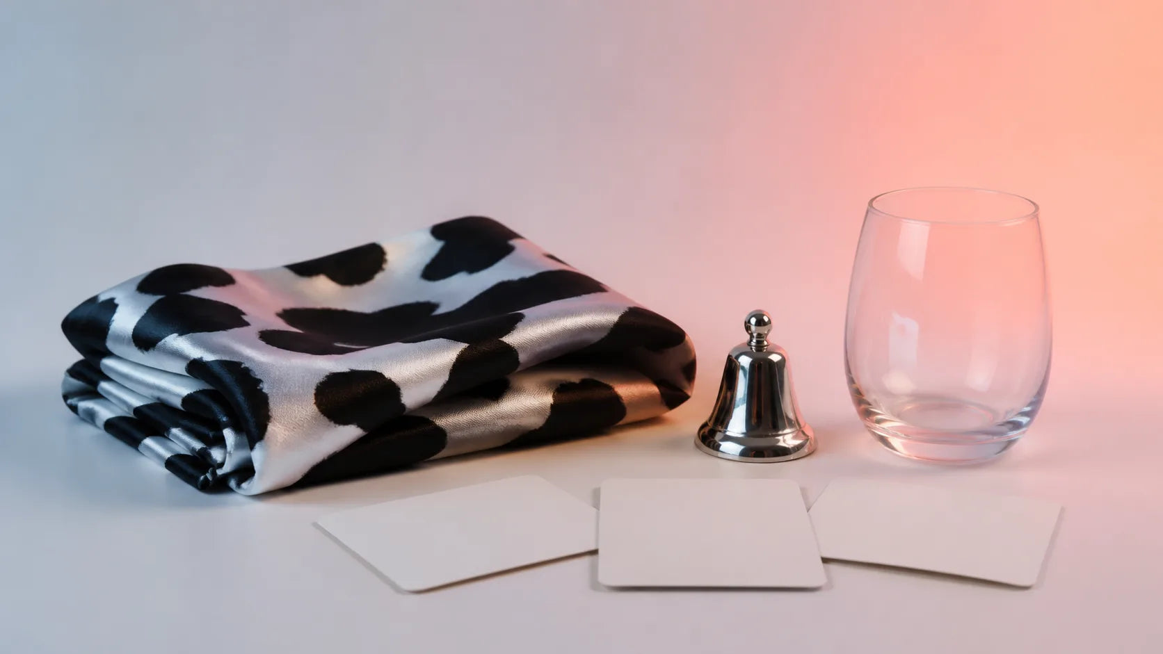 Cow-print textile, silver bell, empty glass and blank planning cards on a cool coral-lit background