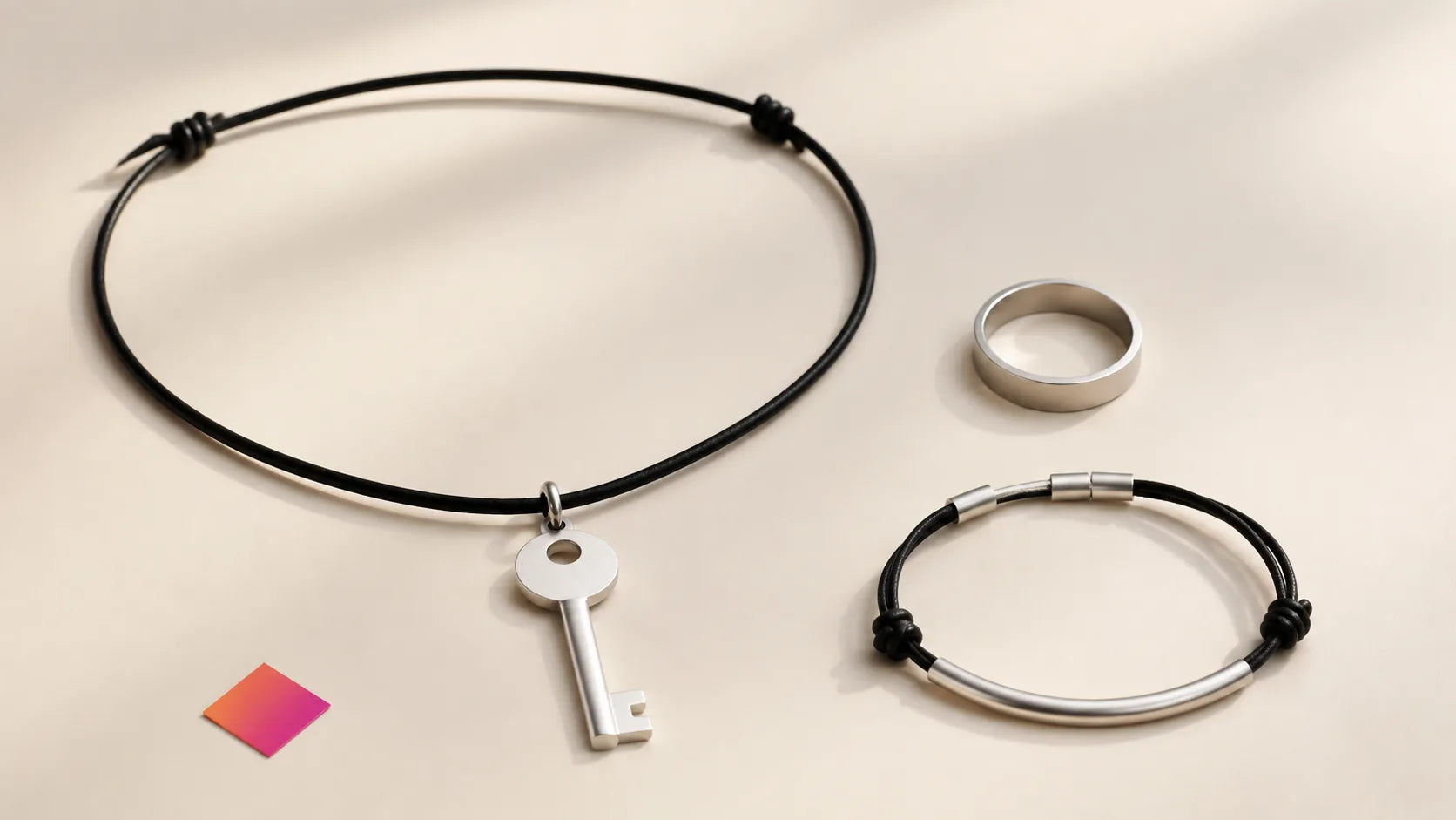 Silver key pendant, black choker-style necklace, ring and bracelet on a warm ivory surface.