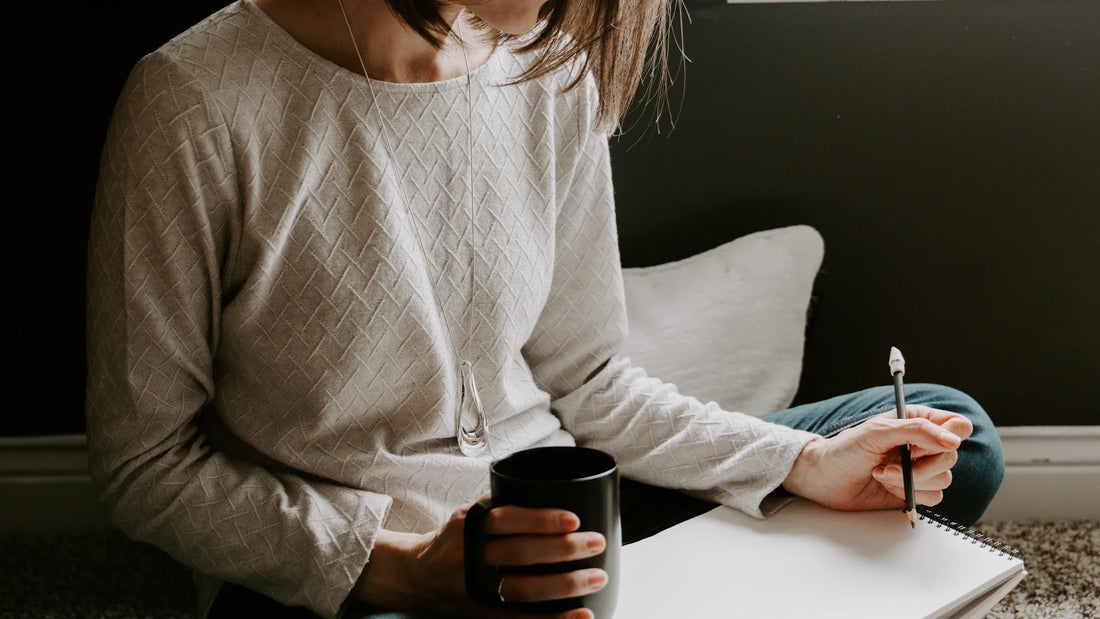 A woman's hand writing in a notebook beside a coffee cup.