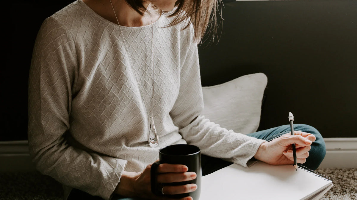 A woman's hand writing in a notebook beside a coffee cup.