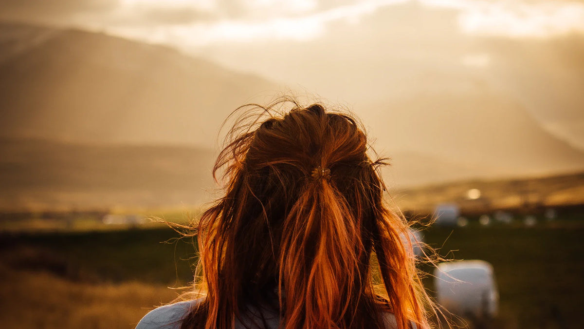 A woman seen from behind looking across a sunlit field.