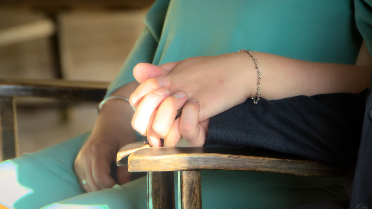Two adults holding hands beside a wooden chair, with faces outside the frame.