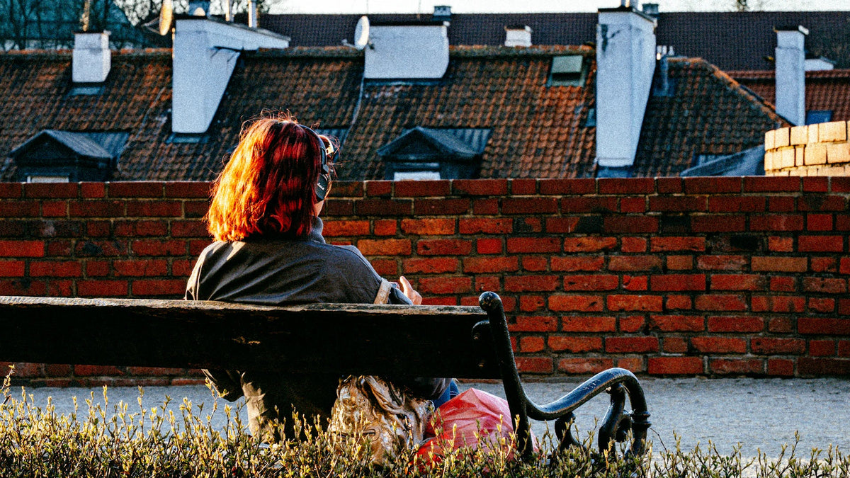 A red-haired woman sits on a bench wearing headphones.