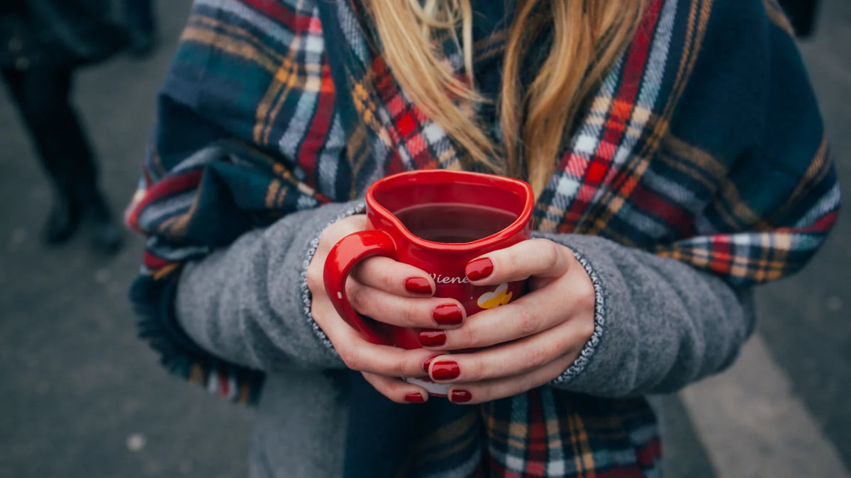 An adult woman holding a red mug in both hands, with her face outside the frame.