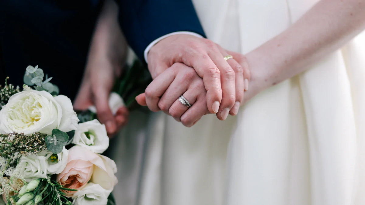 A close-up of adult hands resting together beside a white floral bouquet.