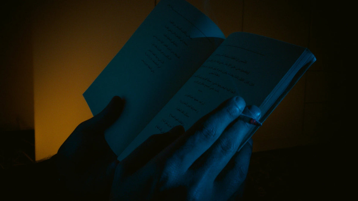 Hands hold an open book in blue light.