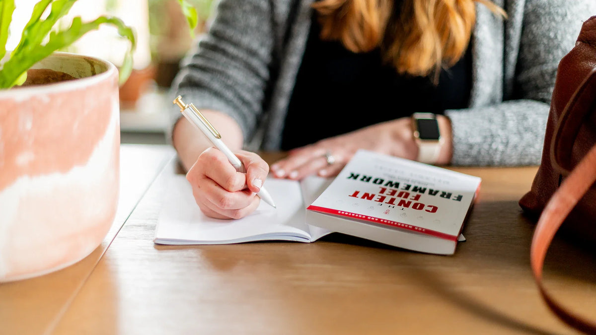 A woman takes notes at a table, with her face outside the frame.