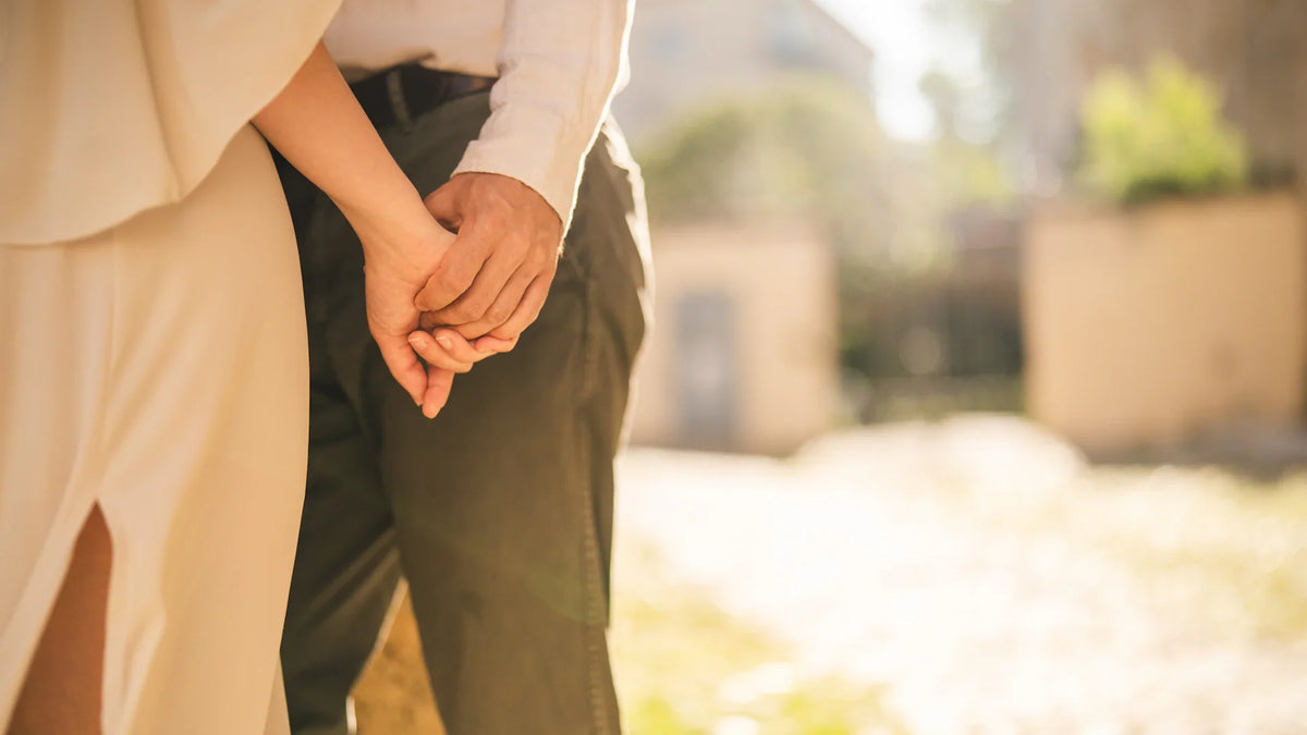 Two adults holding hands outdoors in warm sunlight, with their faces outside the frame.