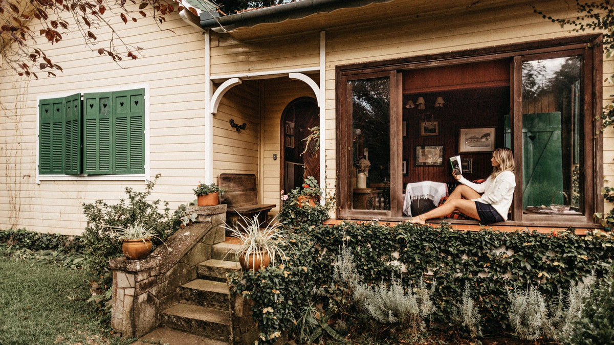 A woman reading a book in the window of a house.