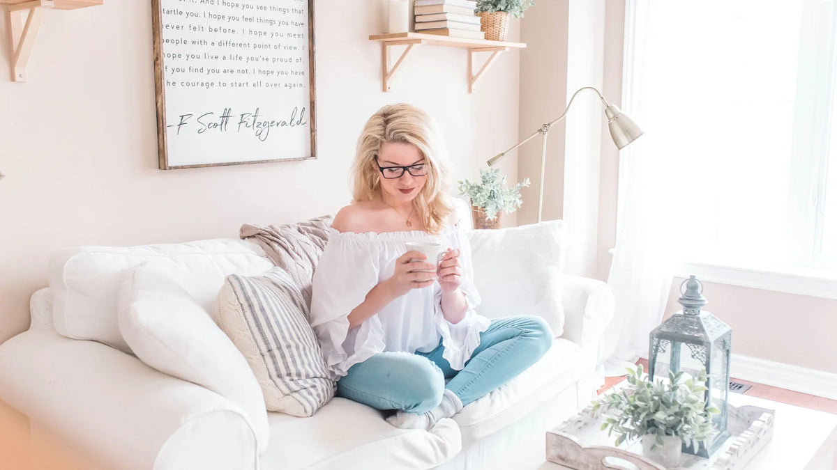 A woman sits comfortably on a sofa with a mug.