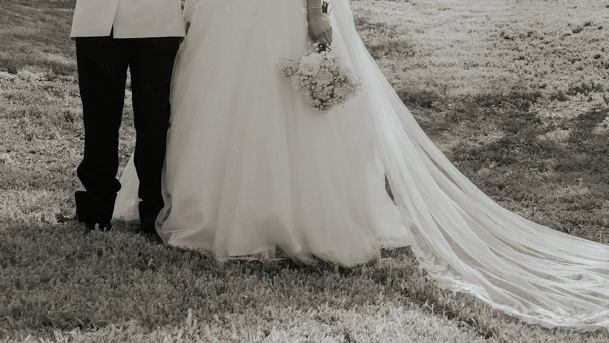 Wedding clothes and a bouquet on a couple photographed in a park, with faces outside the frame.